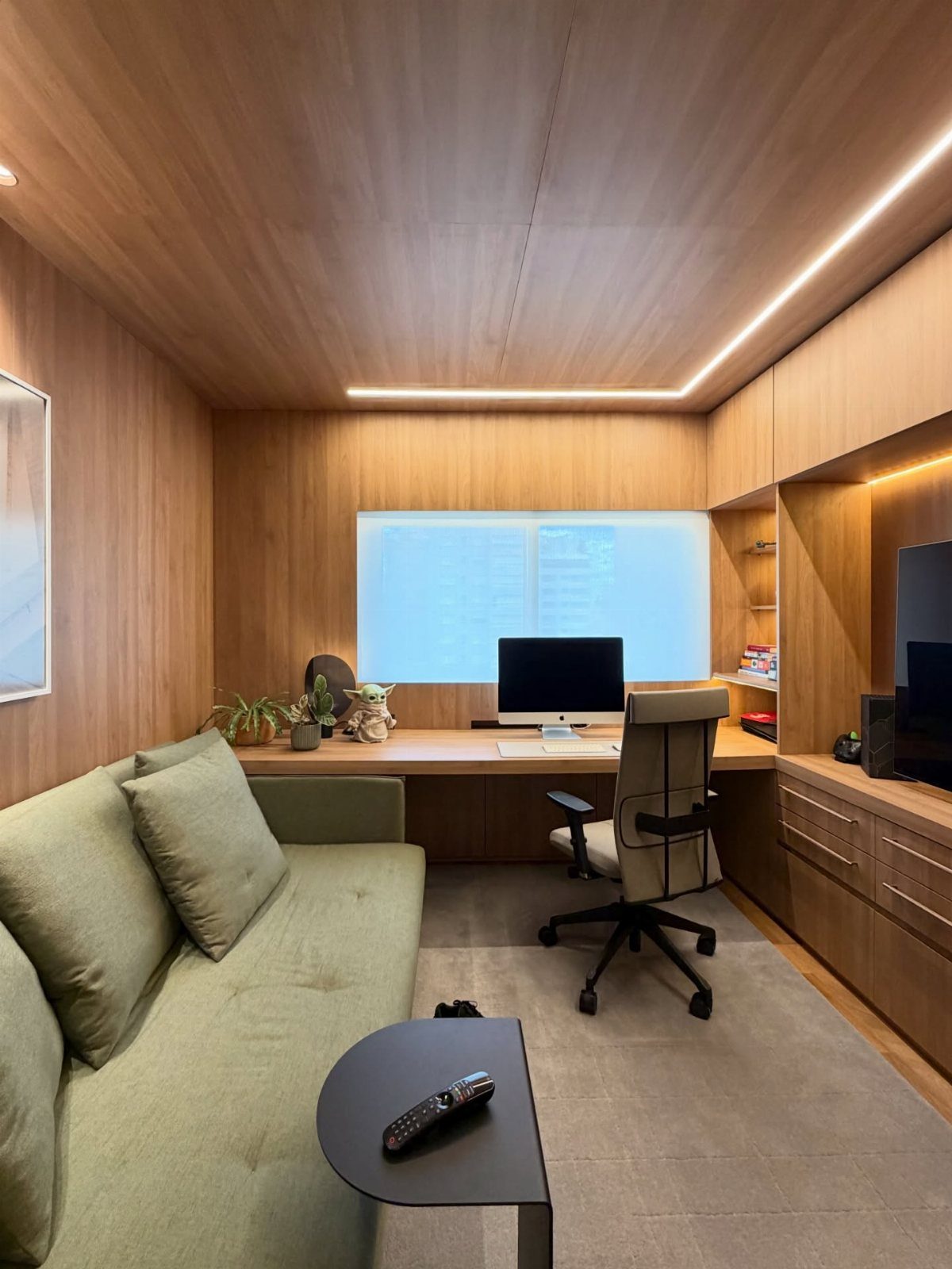Modern home office featuring wood paneling, a long desk with a computer, and a green sofa.