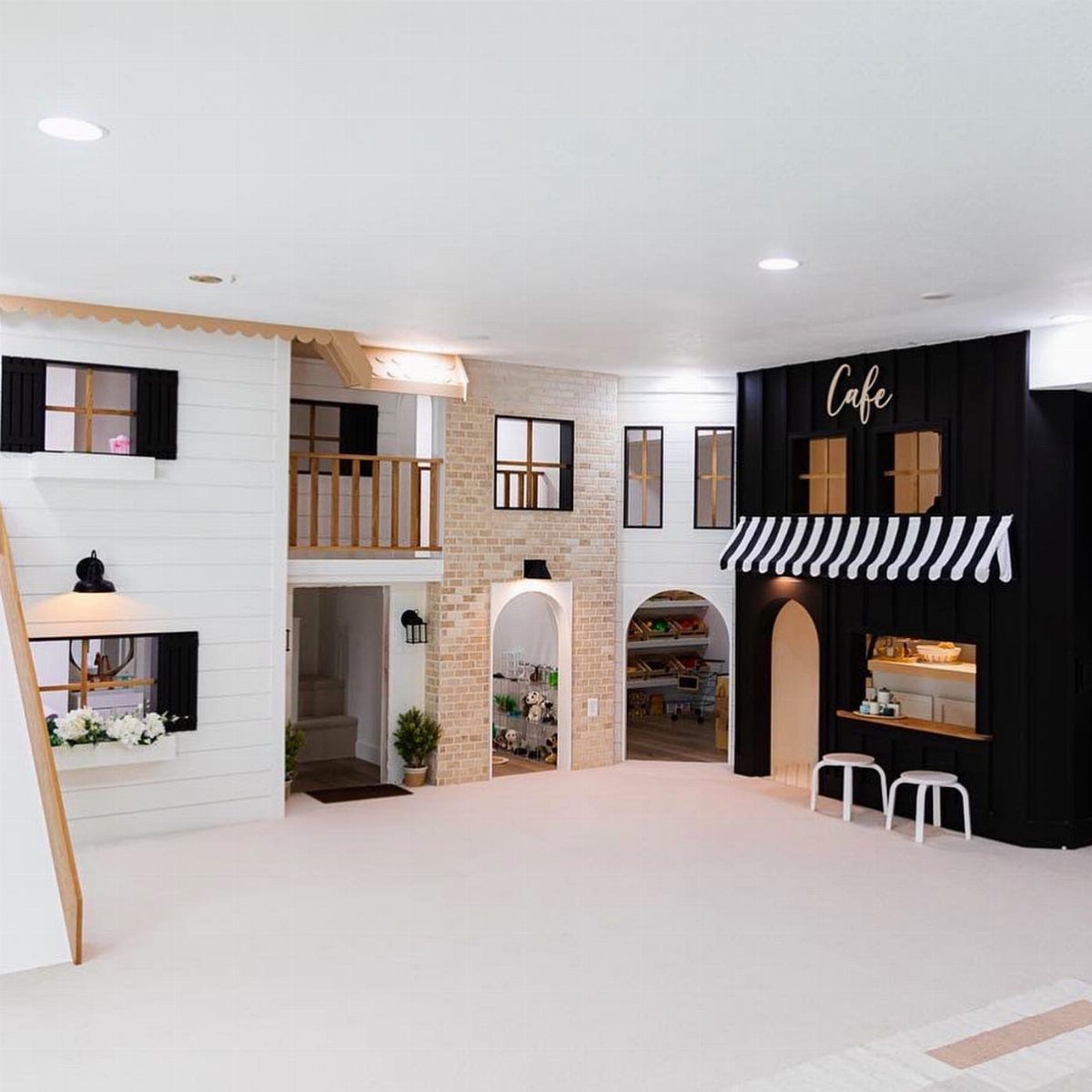 Miniature playhouses including a white wooden house and a black cafe in a bright playroom.
