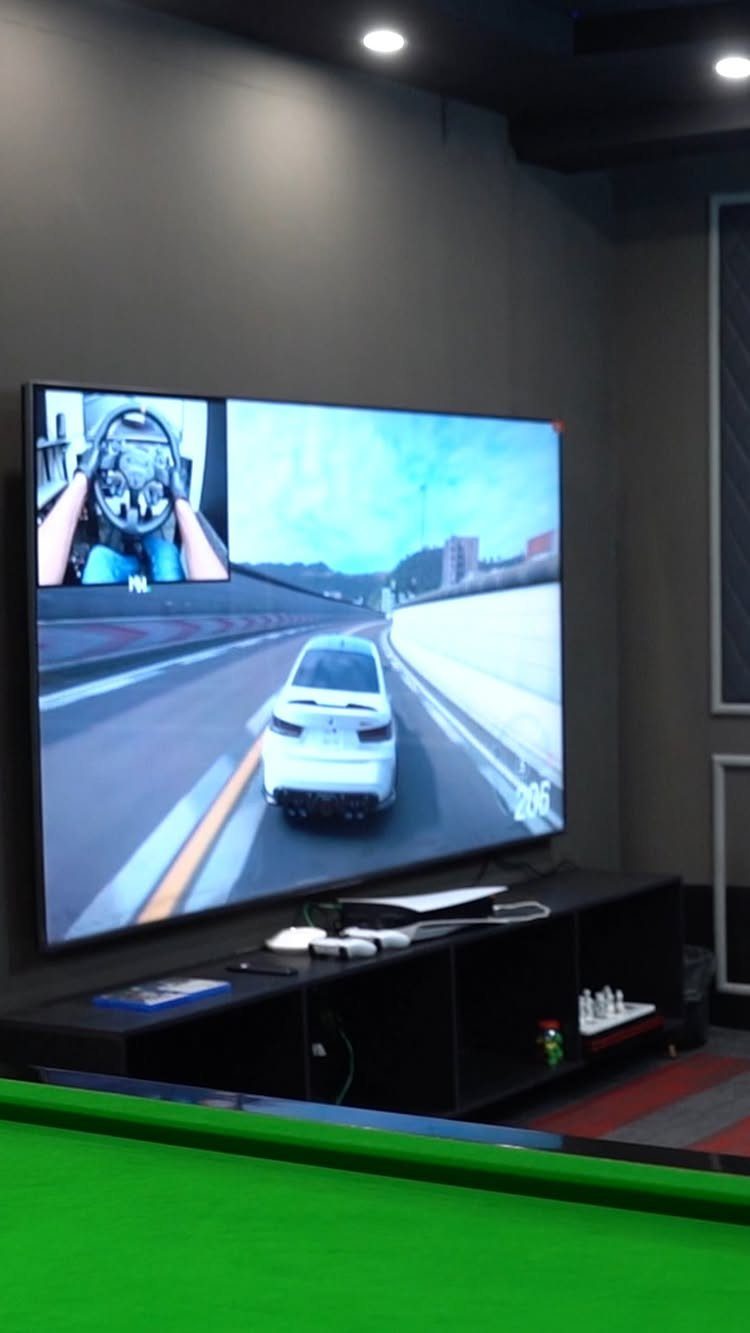A large television screen displaying a racing video game on a black media console.