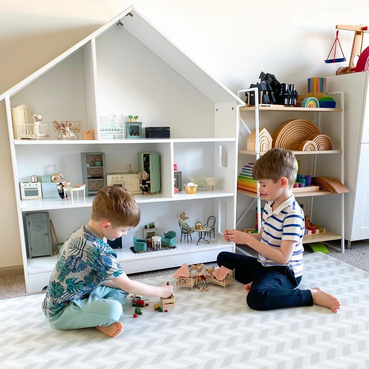 Two young boys playing with wooden toys and a dollhouse on a white patterned rug.