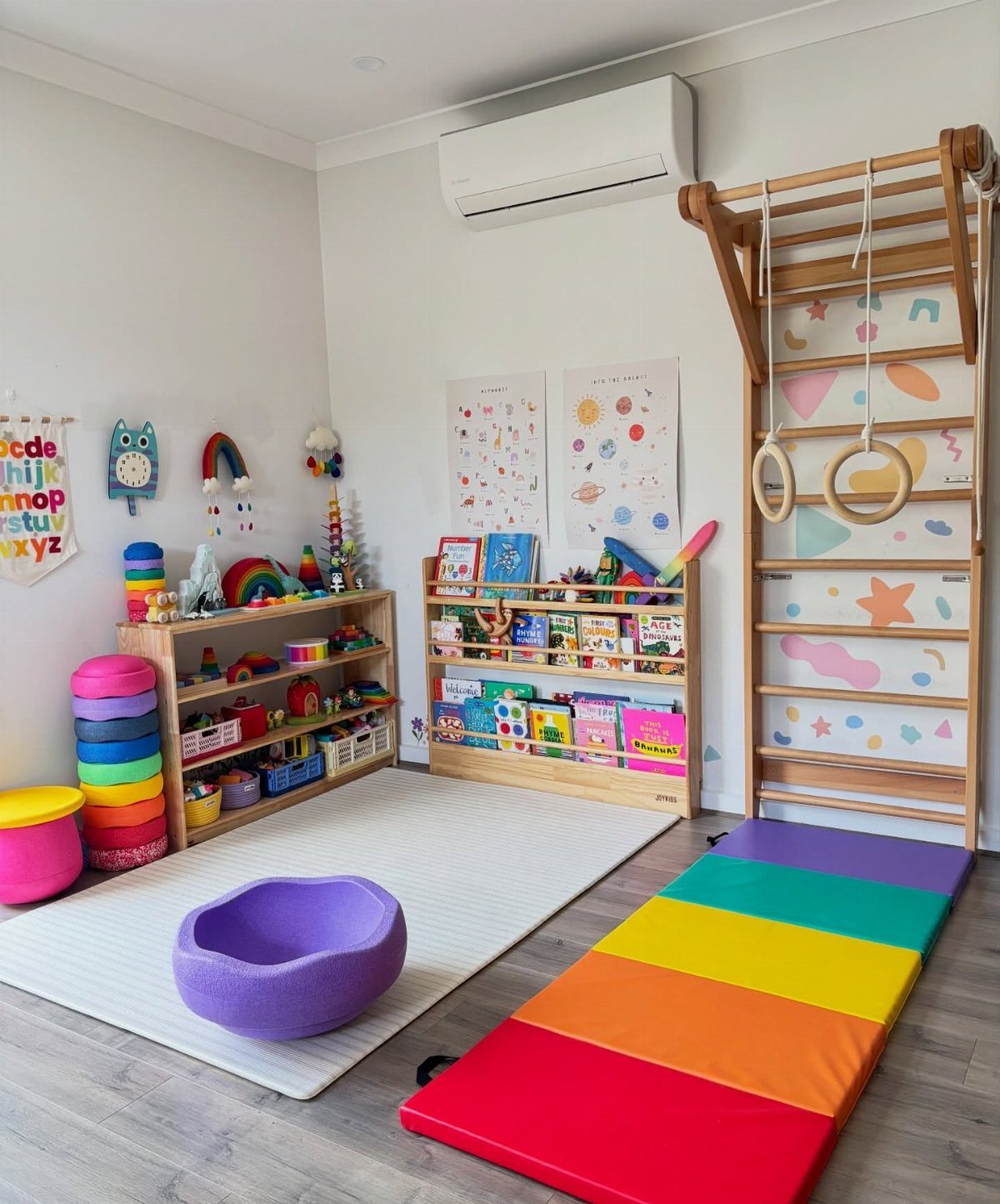 A colorful playroom with wooden toy shelves, a rainbow mat, and a climbing wall with decals.