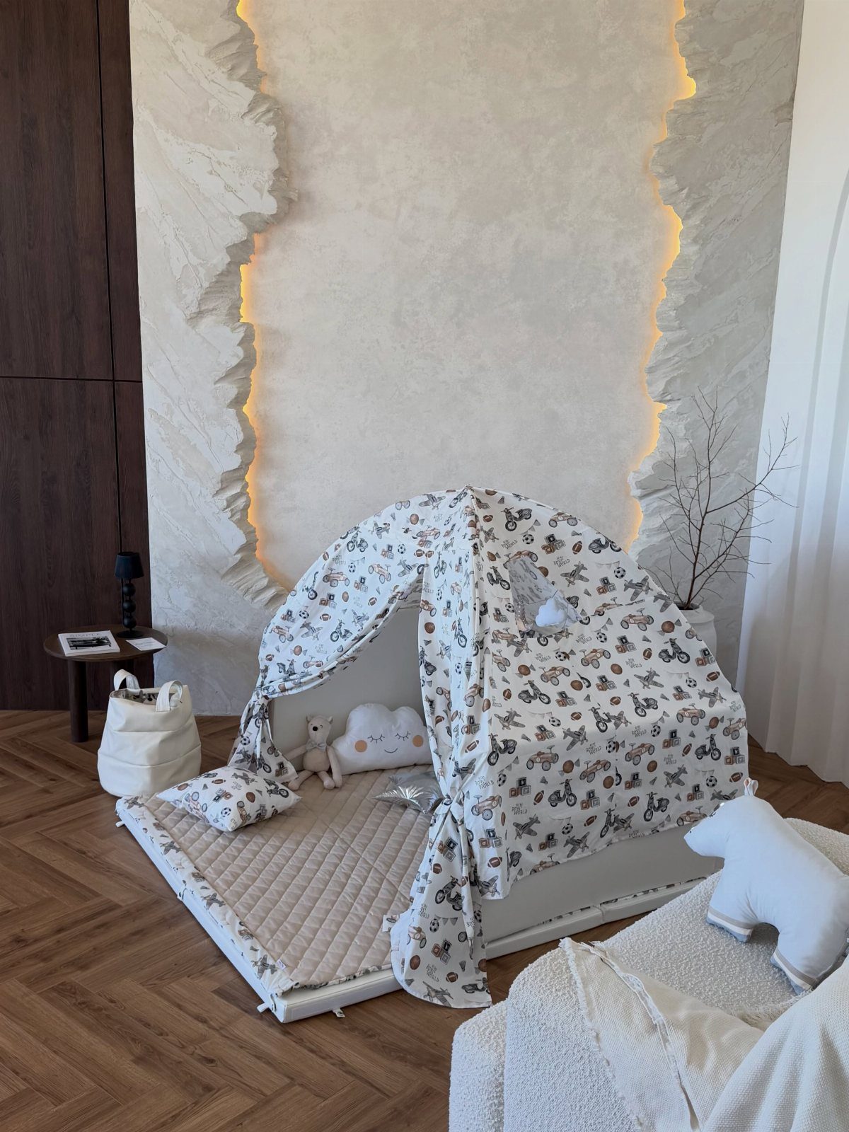 A patterned fabric play tent sits on a quilted mat in a neutral room.