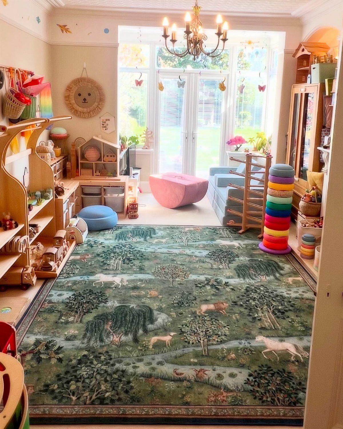 A large green forest-patterned rug with animals covers the floor of a bright, well-lit children's playroom.