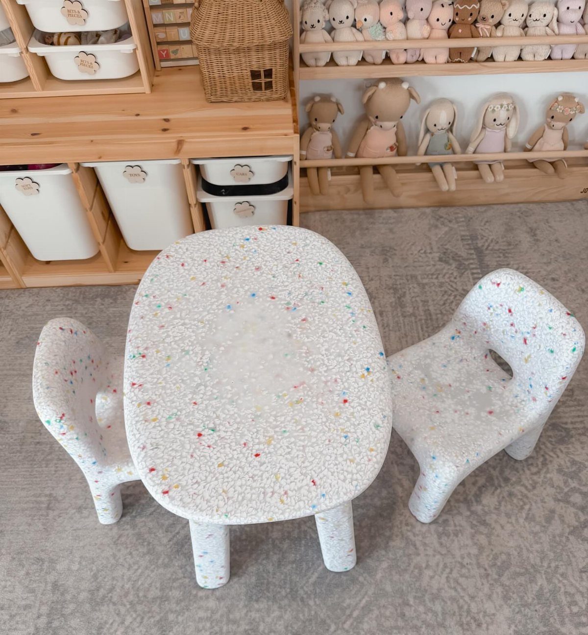 Small white speckled terrazzo child's table and two matching chairs on a grey carpet.
