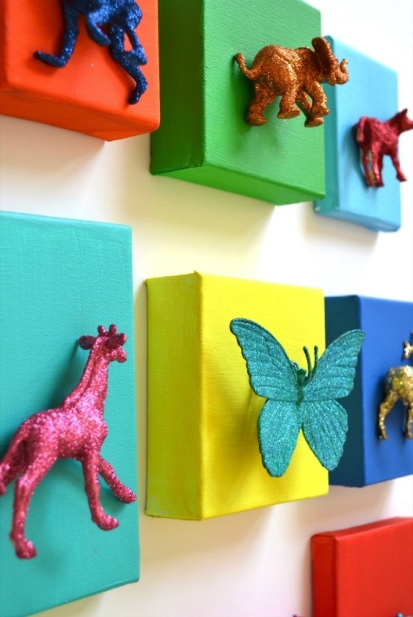 8 DIY Playroom Wall Art Ideas: Projects Kids Help Build 6 Glittery 3D animal figures attached to colorful rectangular canvases mounted on a white wall.