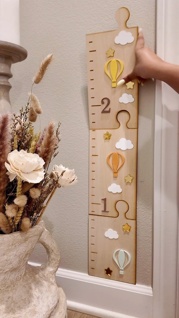 8 DIY Playroom Wall Art Ideas: Projects Kids Help Build 8 A hand touches a wooden hot air balloon themed growth chart mounted on a wall.