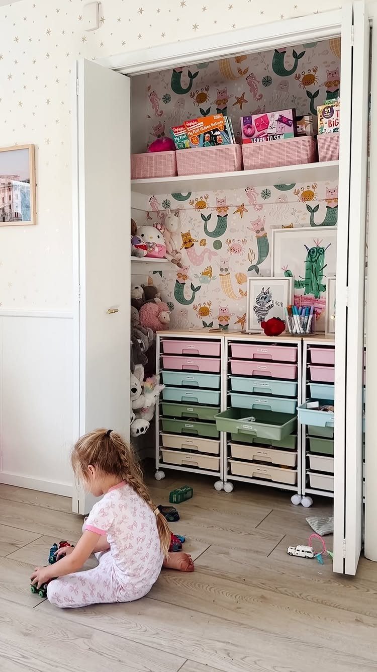 A young child playing on the floor in front of an organized closet filled with colorful toy storage.