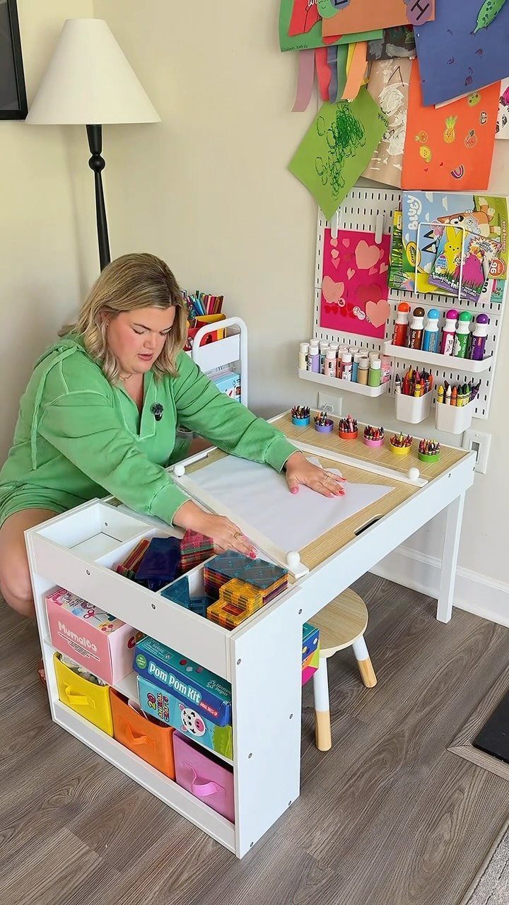 A woman sits at a white craft station table organized with various colorful art supplies.