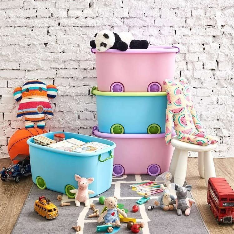 Stacked pink and blue plastic toy bins with wheels surrounded by various stuffed animals and toys.