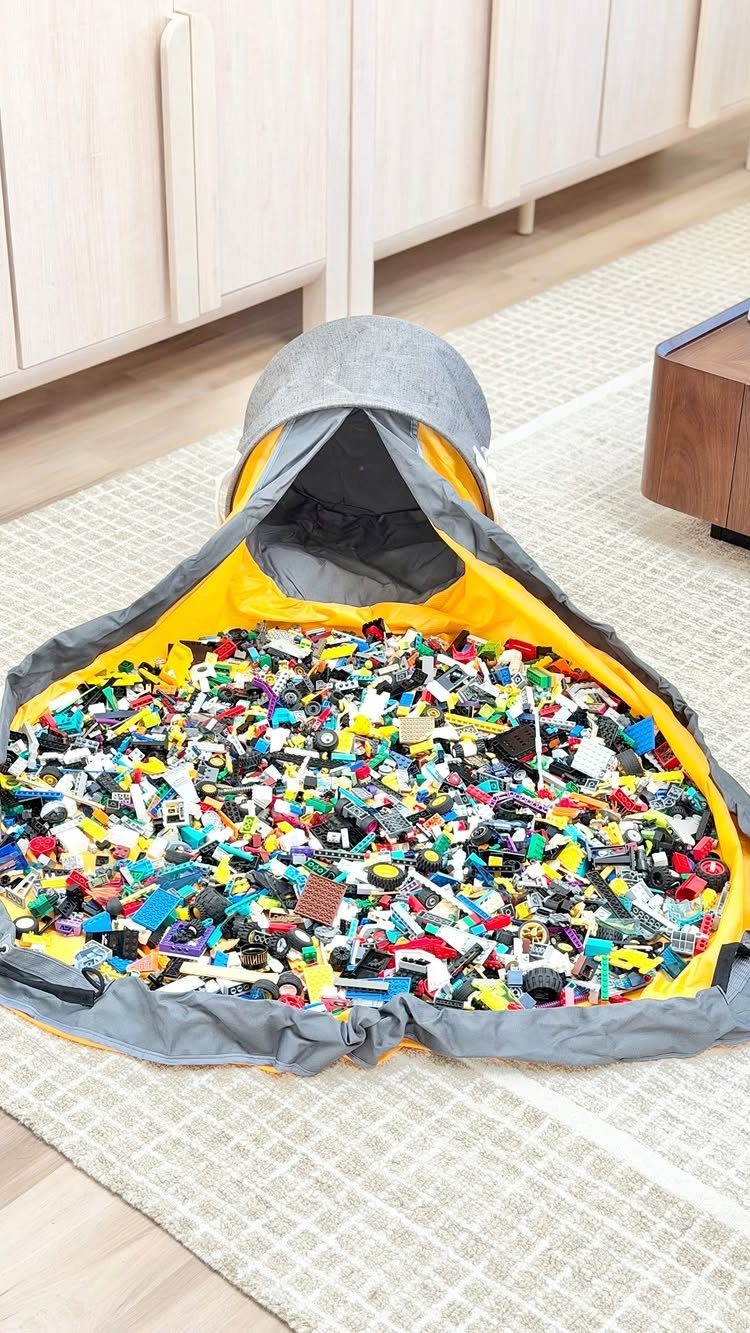 A large grey and yellow drawstring bag overflowing with colorful assorted LEGO bricks on a rug.