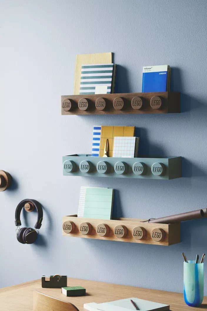 Three colored LEGO wall rack systems holding notebooks and stationery on a blue wall.