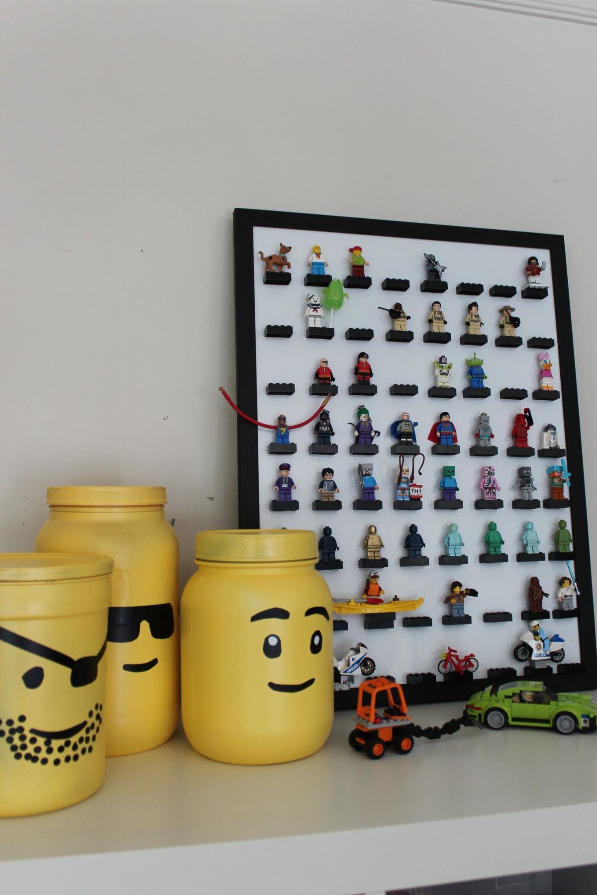 Yellow LEGO minifigure head canisters and a minifigure display frame on a white shelf.