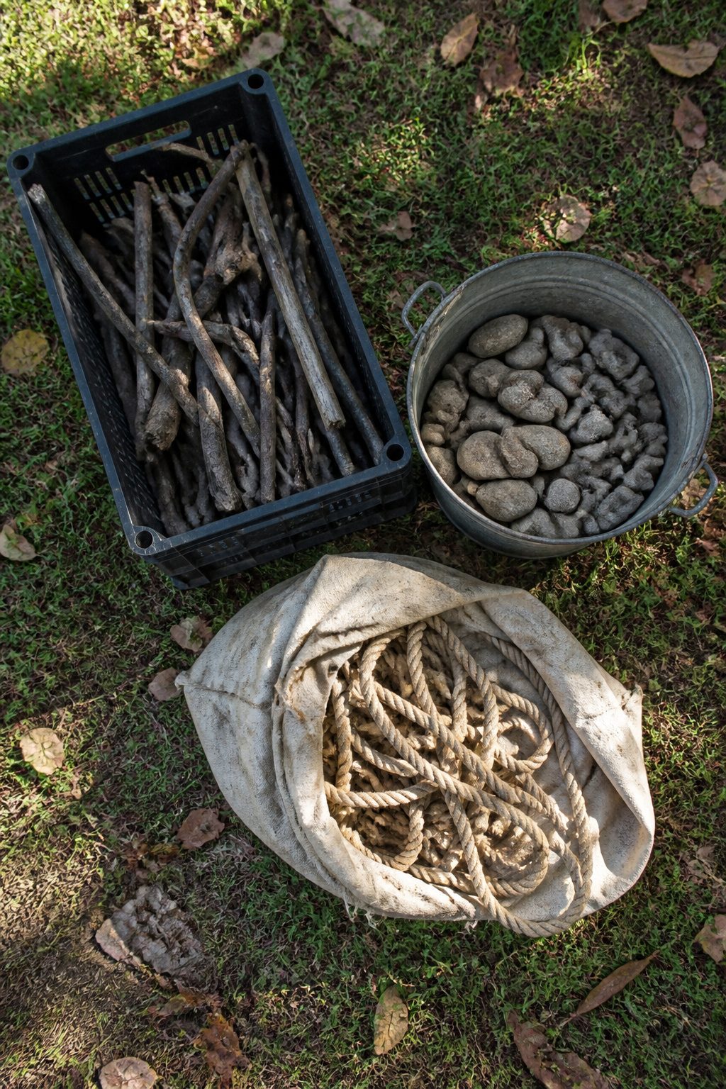 Milk crate with sticks, bucket of stones, and sack of rope.