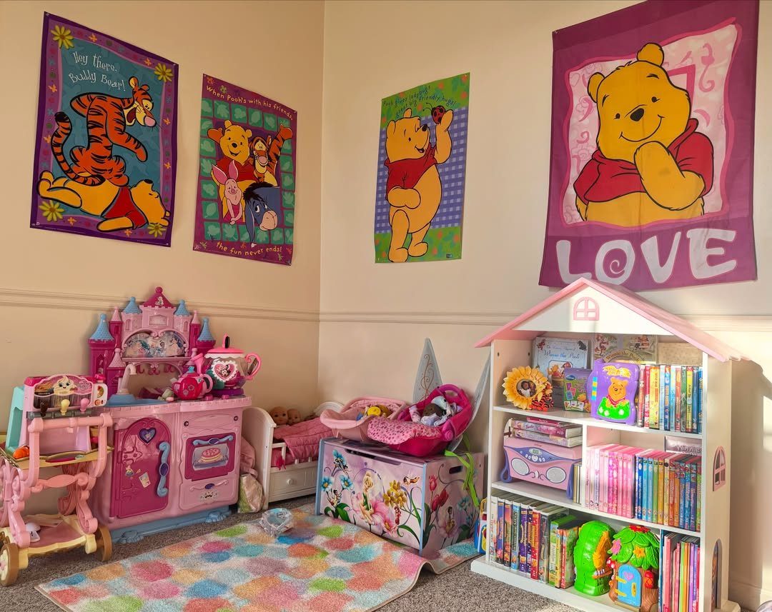 Winnie the Pooh banners hang above a pink toy kitchen and a white bookshelf in a playroom.