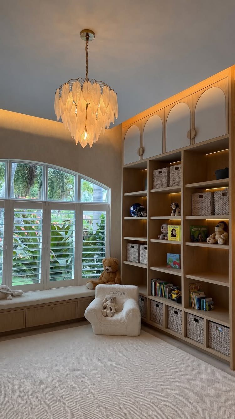 A bright playroom with a large arched window, built-in shelving, and a decorative chandelier.