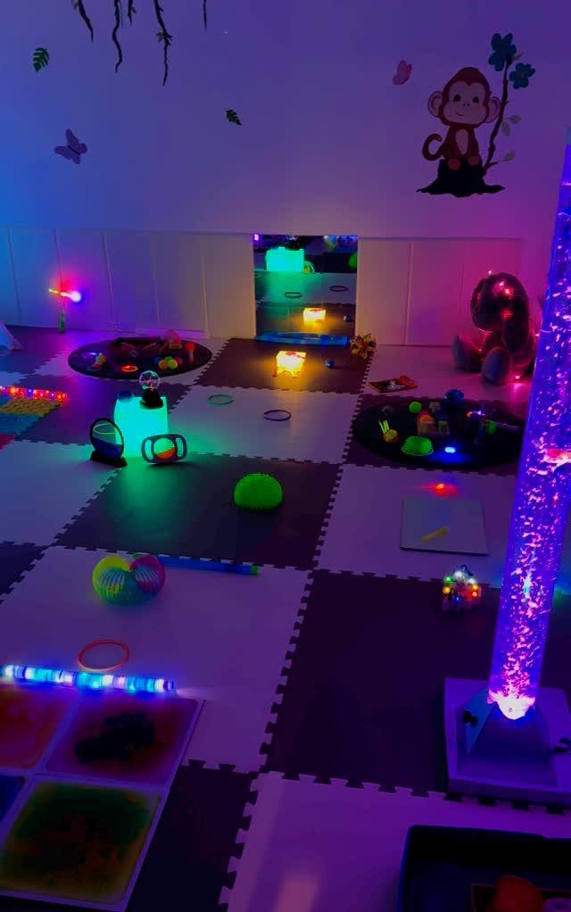 Colorful glowing sensory toys and light-up pillars scattered across interlocking foam play mats in a dark room.