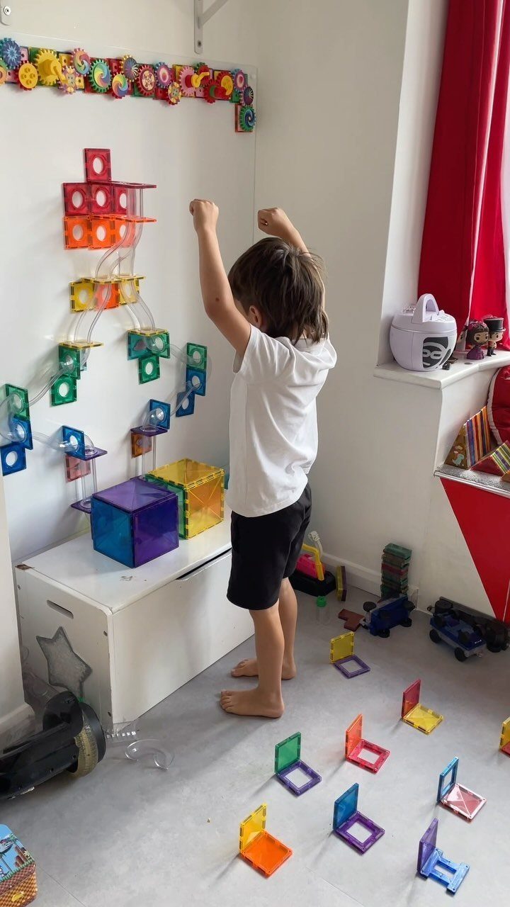 A child playing with colorful magnetic tiles attached to a white playroom wall.