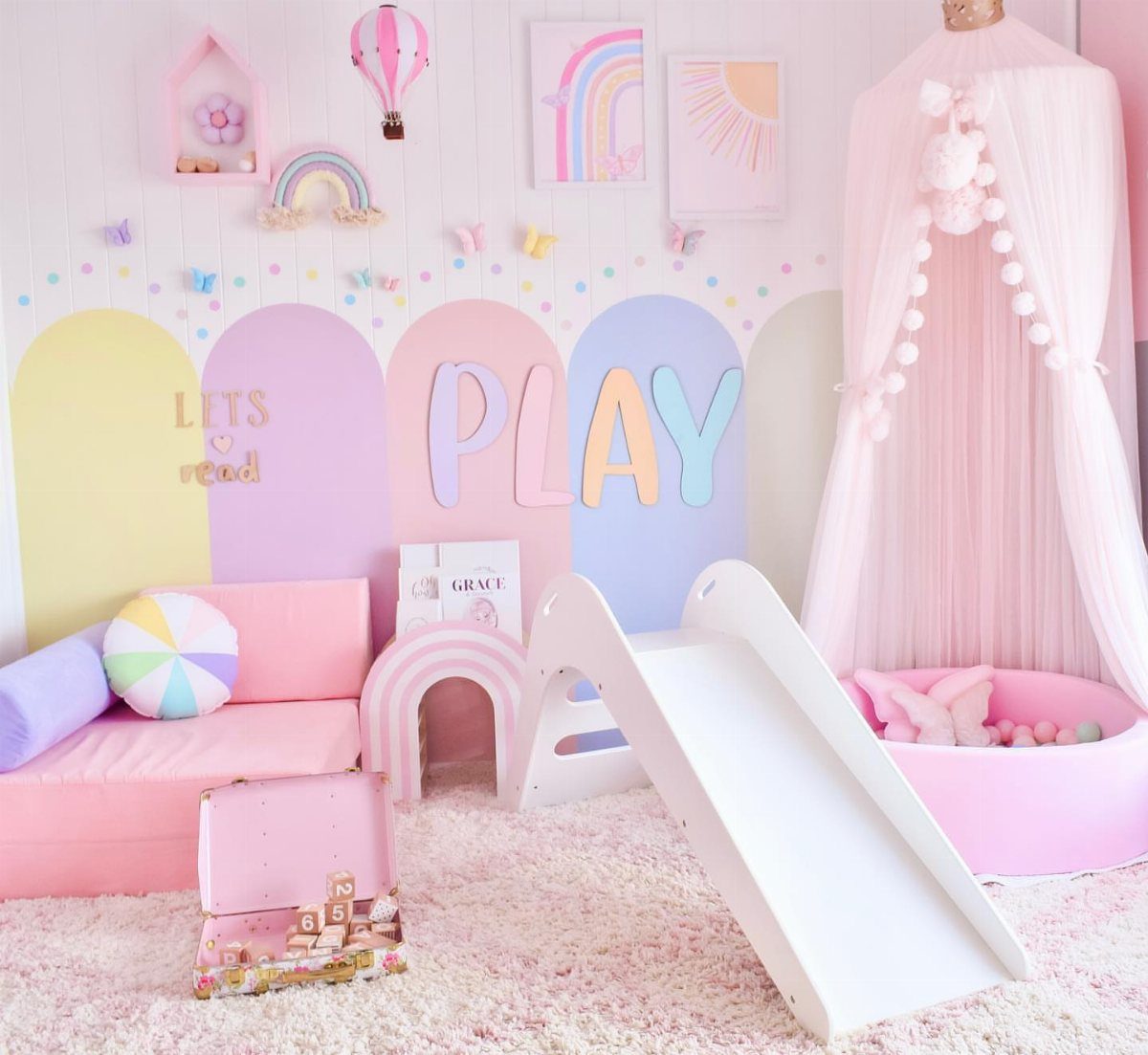 A pastel playroom with arched wall paint, a white slide, and pink furniture on a fluffy rug.