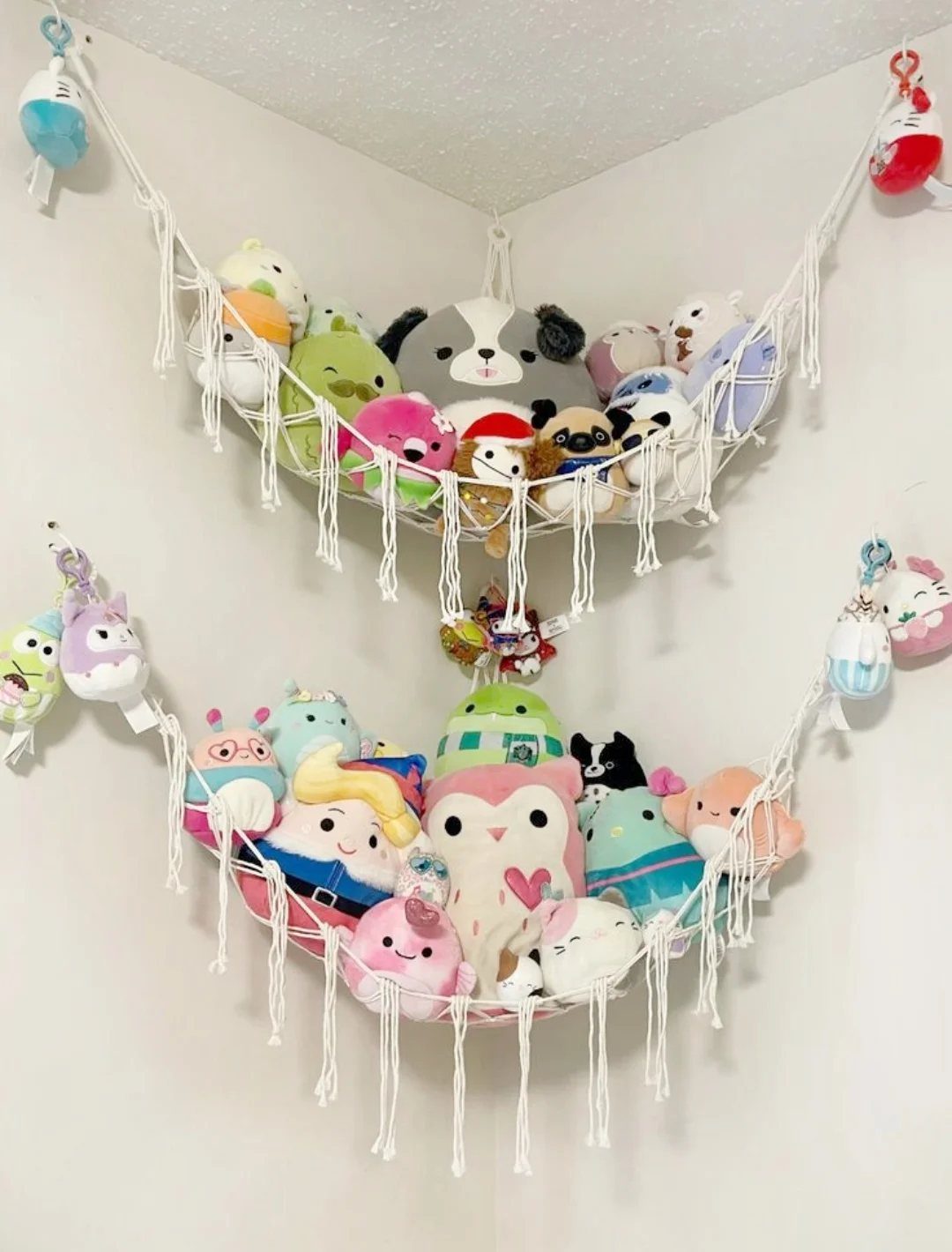 6 Plush Storage Ideas for Stuffed Toys That Clear Floor Pile-Ups 1 Two white macramé hammocks filled with colorful stuffed animals hanging in a room corner.
