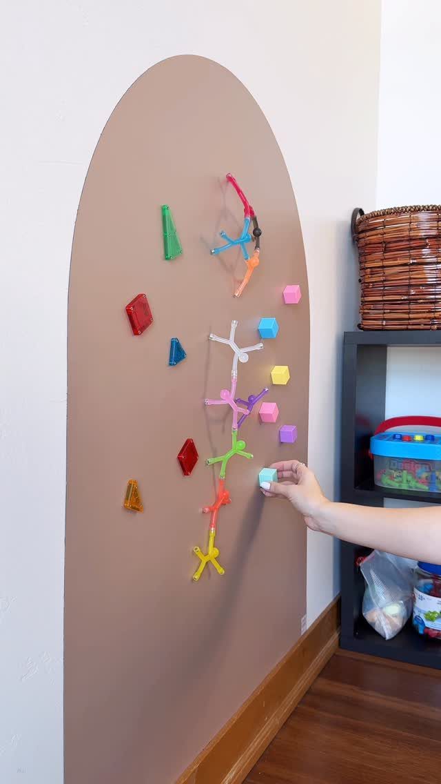 9 Small Play Area Ideas for Families Short on Space 8 A hand placing a small blue cube onto a large tan arched magnetic wall decorated with colorful shapes.