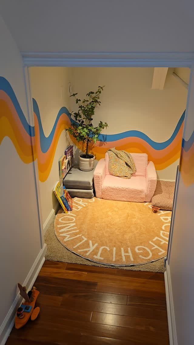 9 Small Play Area Ideas for Families Short on Space 2 A cozy reading nook with a pink armchair, alphabet rug, and wavy patterned walls.