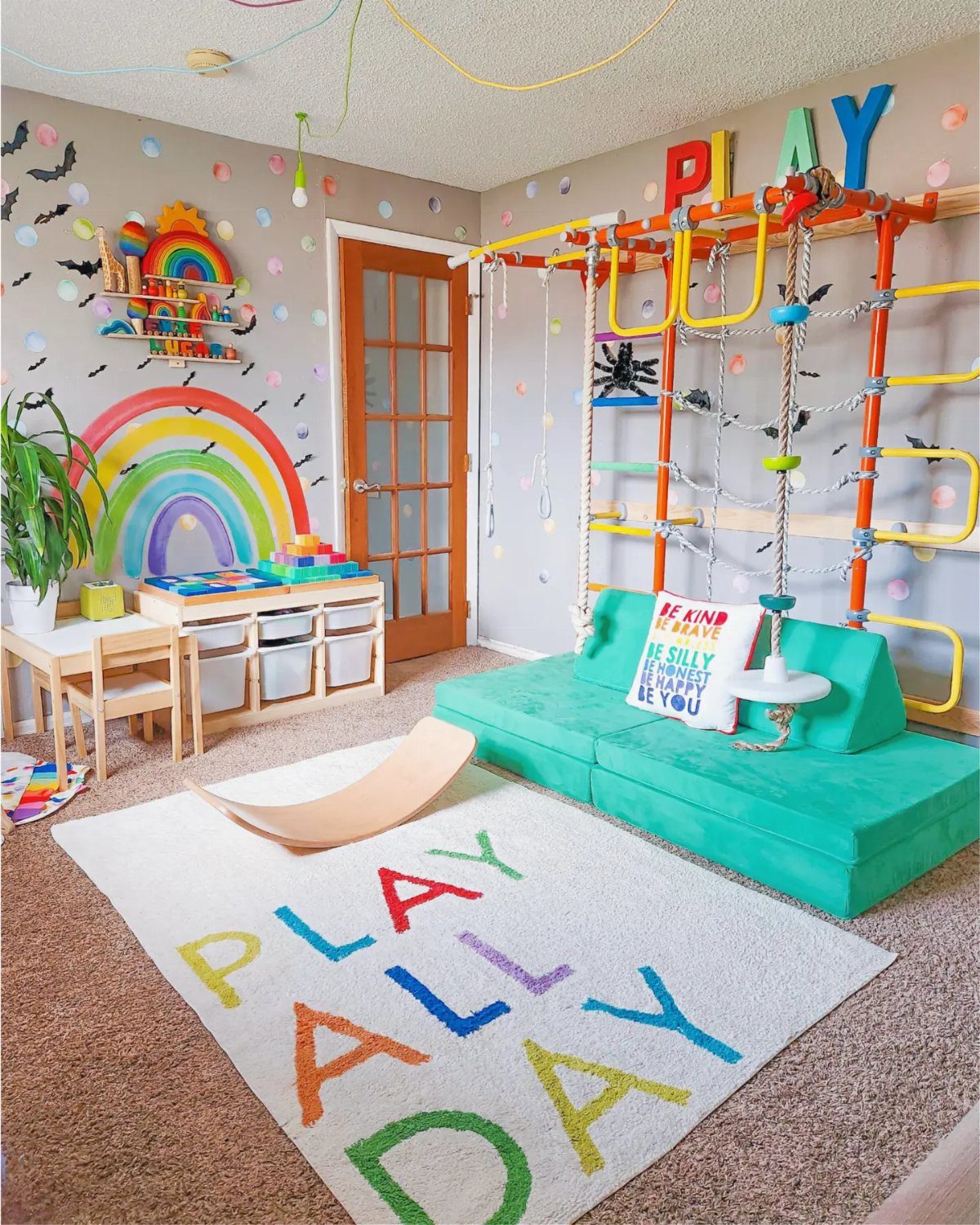 9 Small Play Area Ideas for Families Short on Space 7 Colorful playroom with rainbow wall art, teal modular sofa, and a climbing gym structure.