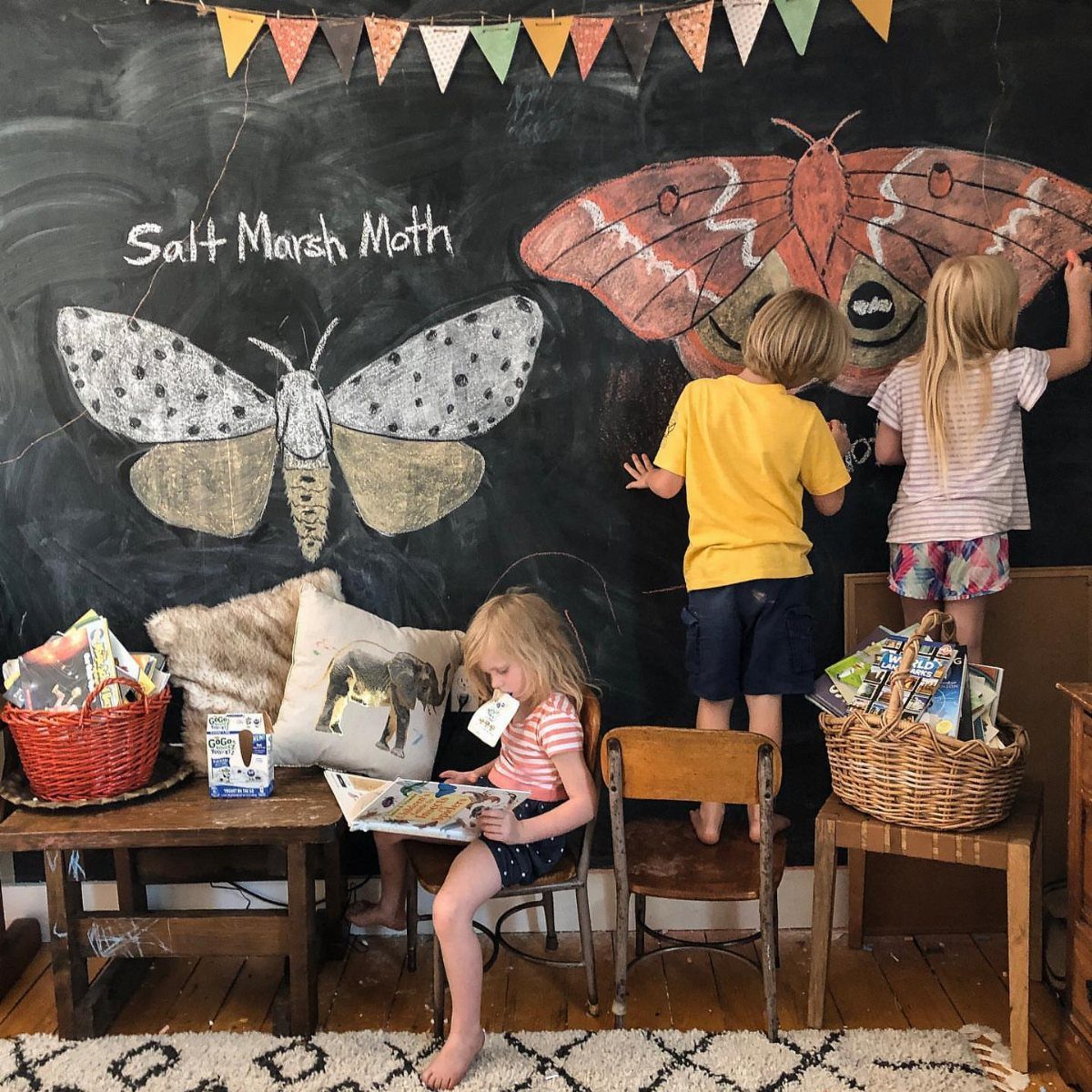 23 Small Playroom Design Ideas That Fit Real Rooms 11 Children drawing large colorful moths on a large black chalkboard wall in a playroom.