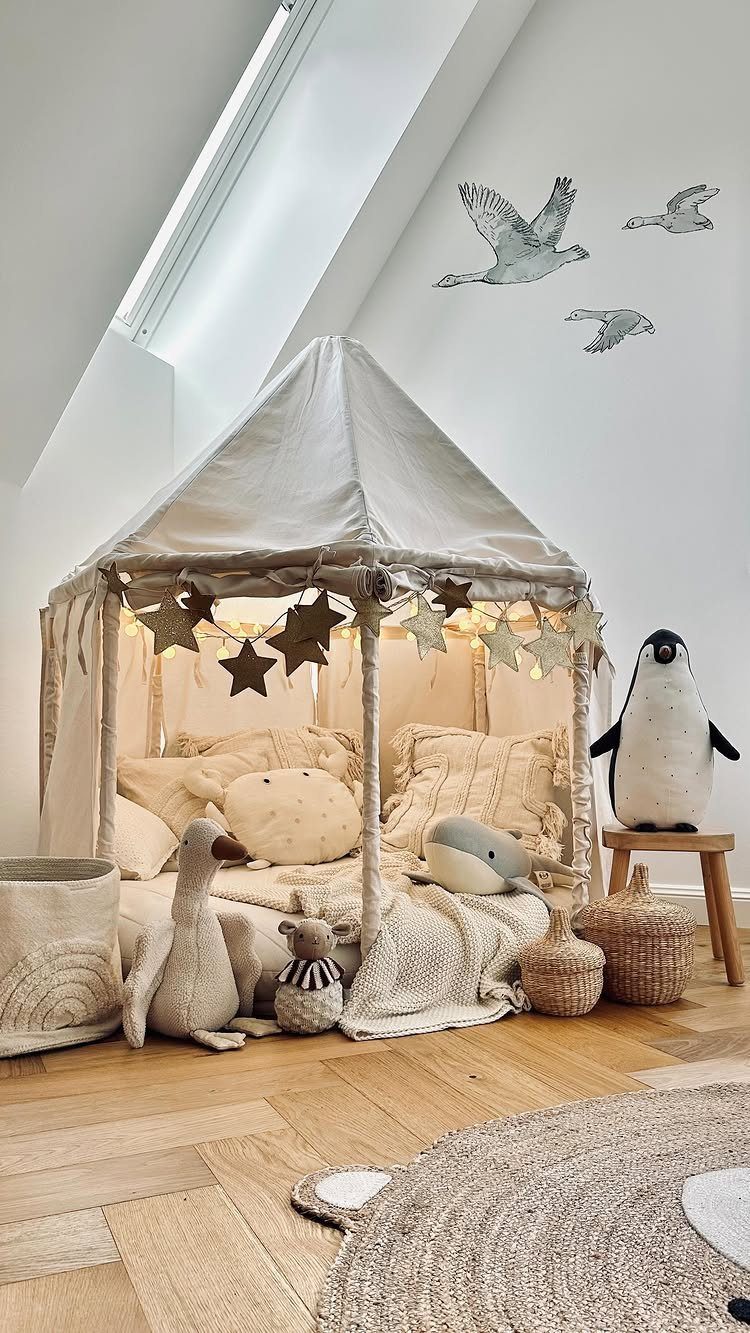 23 Small Playroom Design Ideas That Fit Real Rooms 4 Cream fabric canopy tent filled with soft pillows, blankets, and plush toys on a wooden floor.