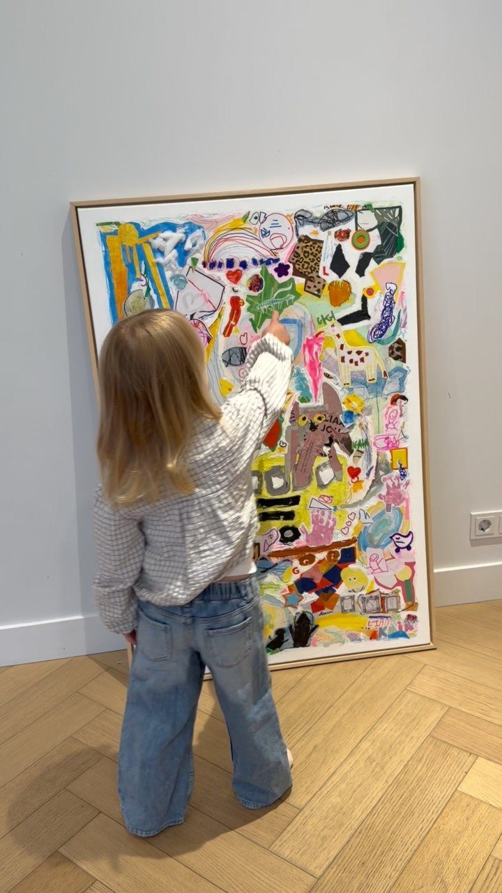 23 Small Playroom Design Ideas That Fit Real Rooms 18 A young child stands before a large, colorful piece of framed abstract art leaning against a wall.