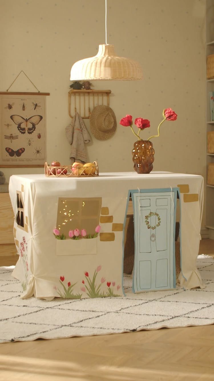 23 Small Playroom Design Ideas That Fit Real Rooms 9 A table covered with a cloth designed to look like a small playhouse with a blue door.