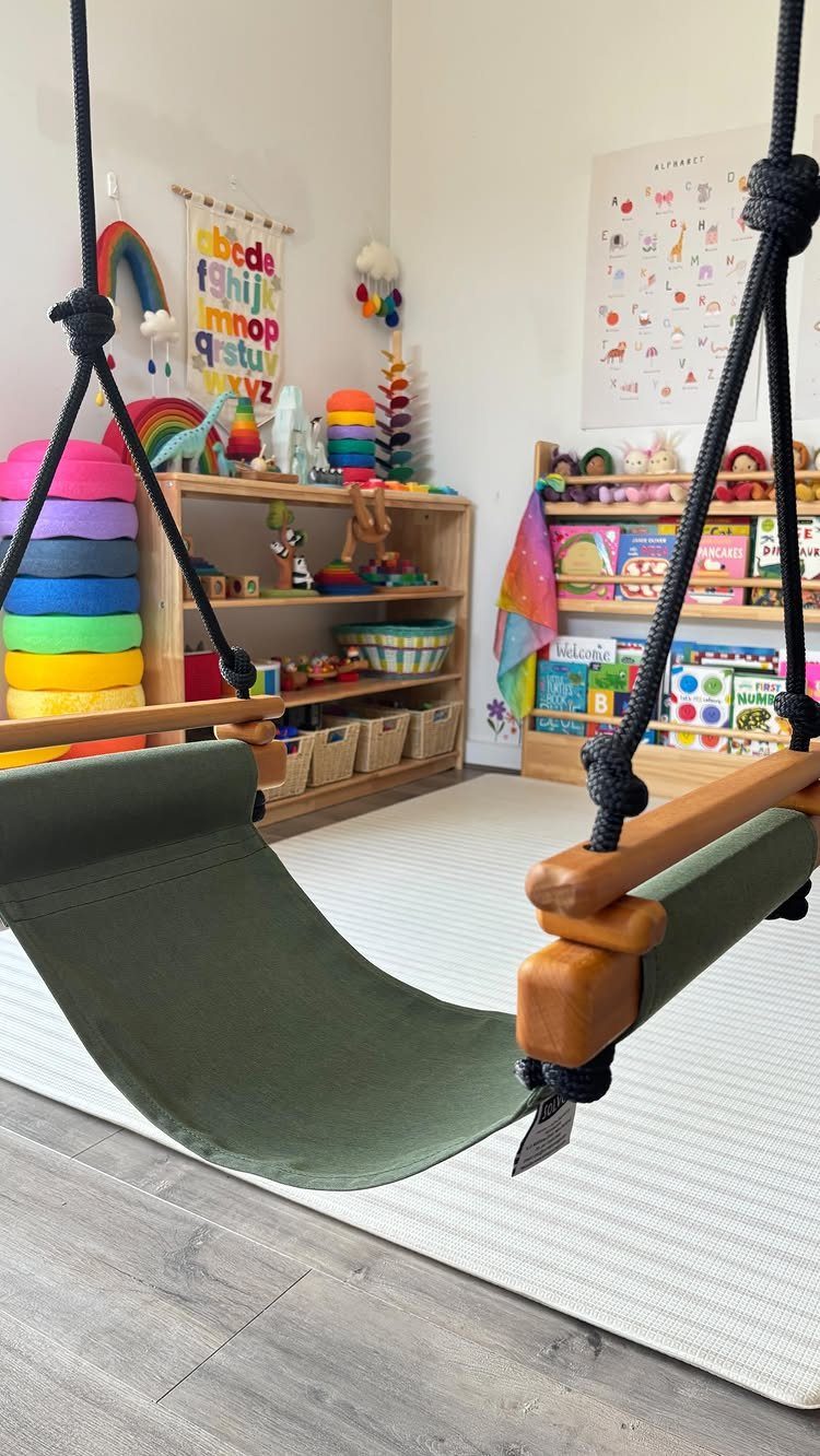 23 Small Playroom Design Ideas That Fit Real Rooms 22 A green fabric hammock swing with wooden handles hangs in a colorful children's playroom.