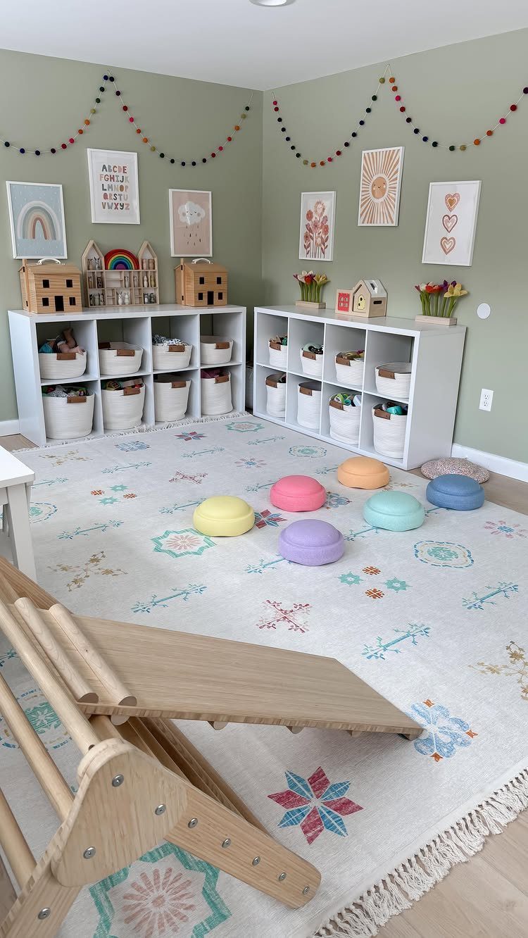 23 Small Playroom Design Ideas That Fit Real Rooms 3 A sage green playroom featuring white storage cubbies, framed wall art, and colorful floor cushions.