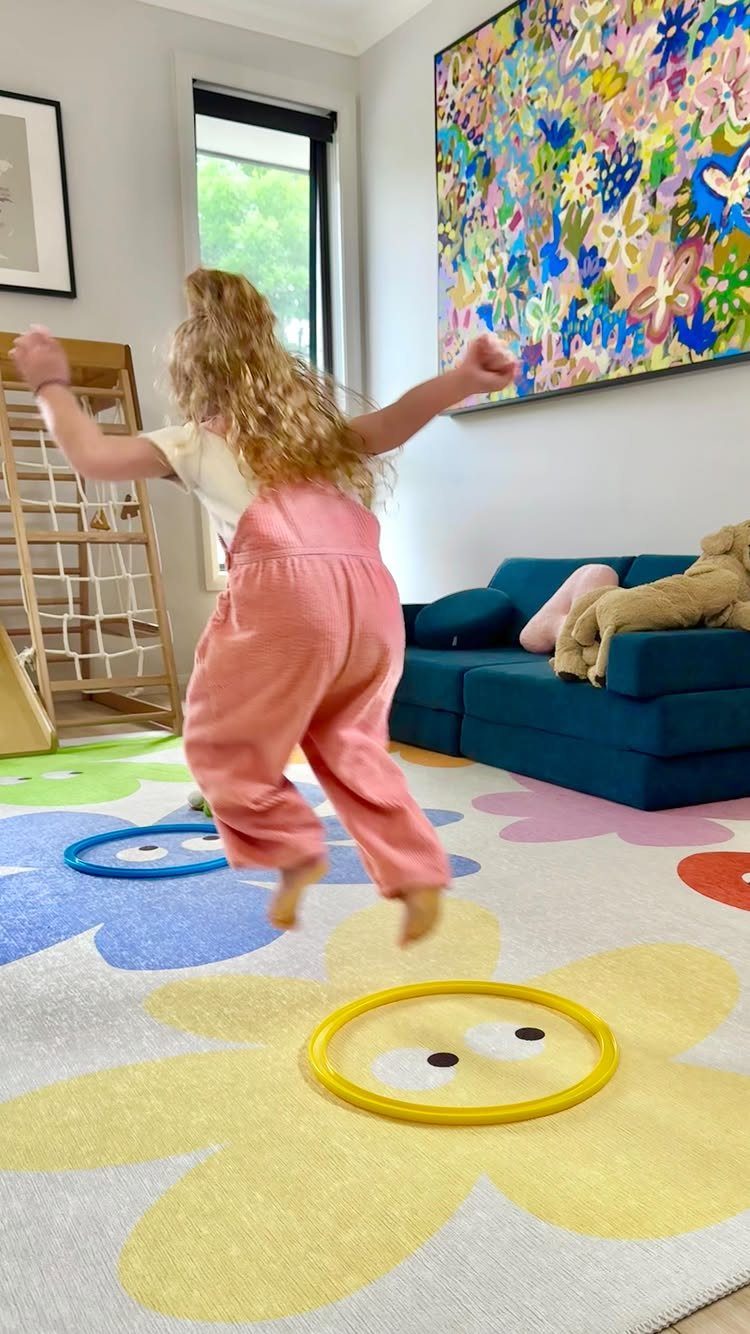 23 Small Playroom Design Ideas That Fit Real Rooms 15 A child jumps on a large white rug decorated with colorful oversized flower patterns.