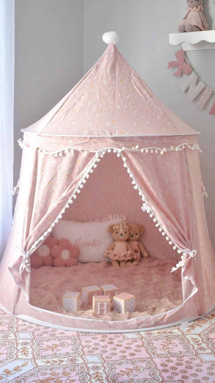 A pink fabric play tent decorated with white pom-poms containing teddy bears and blocks.