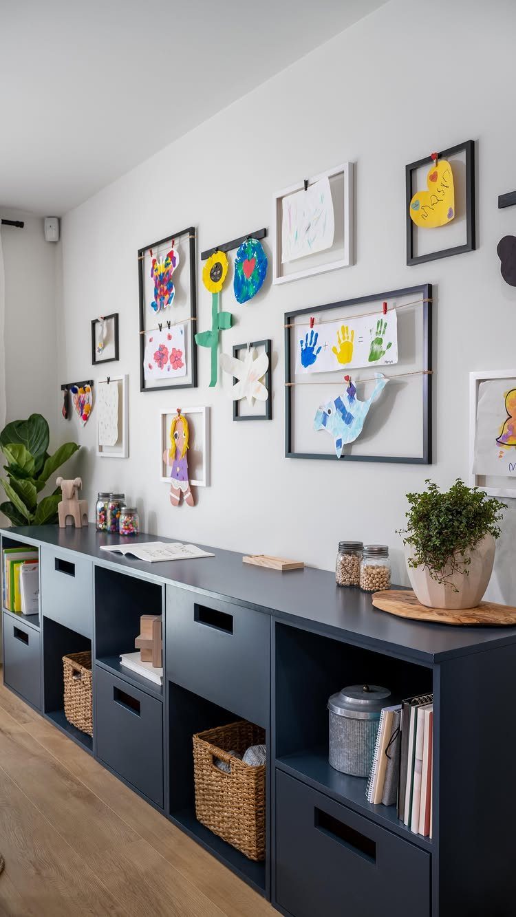 Children's colorful drawings and handprints displayed on a white playroom wall above blue storage units.
