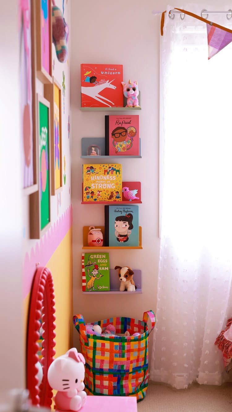 Colorful books on floating shelves next to a patterned storage bin in a bright playroom.